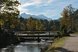 Brücke über einen Bach in einer herbstlichen Parklandschaft mit Bergkulisse im Hintergrund