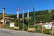 Eingangsbereich eines Freizeit- oder Erlebnisparks mit Fahnen, Informationstafeln und einer umliegenden Berglandschaft