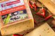 mehrere Stücke Bio-Heumilchkäse mit Verpackung auf einem Holztisch, umgeben von getrockneten Chilis