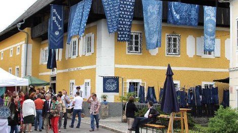 Das Färbermuseum ist ein auffälliges gelbes Gebäude, vor dem sich mehrere Besucher auf einem Platz versammelt haben