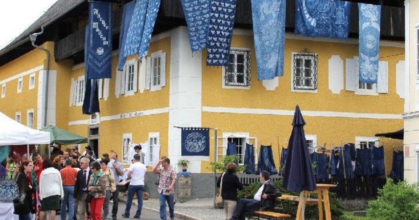 Das Färbermuseum ist ein auffälliges gelbes Gebäude, vor dem sich mehrere Besucher auf einem Platz versammelt haben