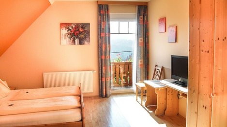 Helles und freundliches Gästezimmer mit gemütlichem Bett, Sitzecke sowie Balkonzugang und schönem Ausblick ins Grüne