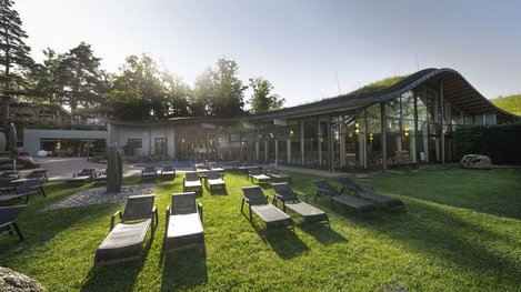 Liegestühle auf einer Grünfläche vor einem modernen Wellnessgebäude im Freien