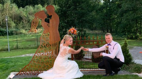 Brautpaar steht vor einer Skulptur in einer Gartenanlage