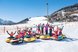 Eine Gruppe Kinder jubelt mit bunten Schneerutschreifen auf einer verschneiten Skipiste