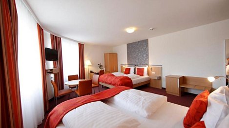 Modernes Hotelzimmer mit mehreren Betten, Sitzbereich und großen Fenstern