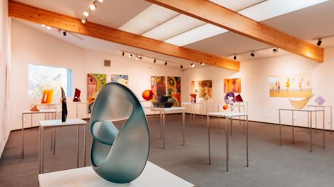 Eine moderne Galerie mit Skulptur, Kunstwerken und warmen Holzbalken an der Decke