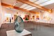 Eine moderne Galerie mit Skulptur, Kunstwerken und warmen Holzbalken an der Decke