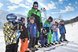 Eine Gruppe von Kindern posiert mit ihrem Skilehrer auf einer verschneiten Skipiste