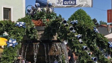 Ein festlich geschmückter Brunnen mit blau-weißen Dekorationen steht im Mittelpunkt eines Marktes in Gutau