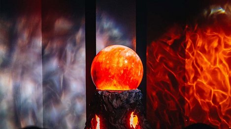 Eine leuchtende orangefarbene Kugel steht vor einer Wand mit feurigen Lichtmustern