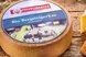 Runder Bio-Bergkräuterkäse mit Kräuterrand auf einem rustikalen Holztisch präsentiert