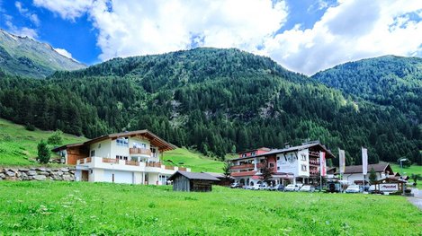 Ein idyllisches Alpenhotel liegt auf einer grünen Wiese vor einer beeindruckenden Bergkulisse