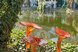 Künstlerische Glasinstallation mit leuchtend orangefarbenen Glasobjekten in einer natürlichen Garten- und Teichlandschaft