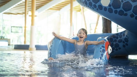 Kind rutscht in einem Hallenbad aus einer Wasserrutsche ins Wasser