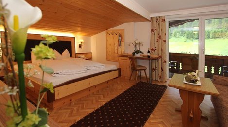Ein gemütliches Zimmer mit Balkon, viel Holz und behaglicher Atmosphäre lädt zum Entspannen und Wohlfühlen ein