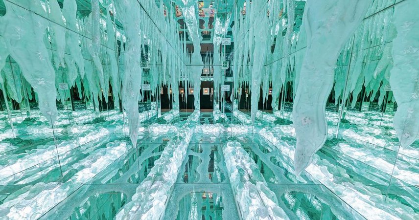 Spiegelnder, türkisfarbener Raum mit reflektierenden Flächen und hängenden, eisähnlichen Glaselementen in kunstvoller Anordnung
