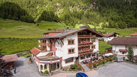 Ein gemütliches Hotel liegt eingebettet in einer grünen Berglandschaft mit Wiesen und Wäldern