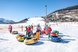 Eine Gruppe Kinder steht mit bunten Schneerutschreifen auf einer verschneiten Piste