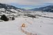 Eine verschneite Skipiste mit Absperrungen in einem weiten Bergtal
