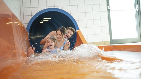 Kind und zwei Erwachsene rutschen gemeinsam eine Wasserrutsche hinunter